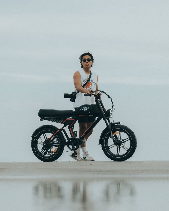 A young man in sunglasses stands with his electric bike on the beach in Miami, Florida.