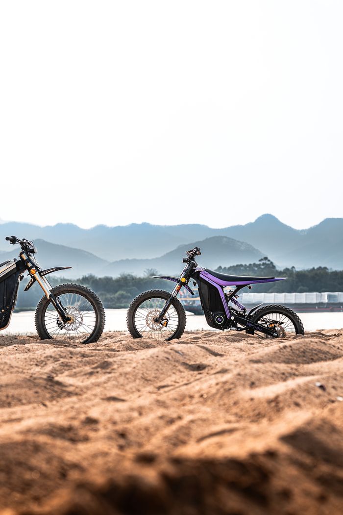 Modern electric bikes parked on a sandy beach with scenic mountain backdrop.